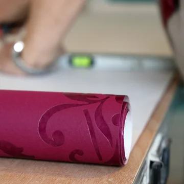 Auf einem Tapeziertisch wird eine Mustertapete abgeschnitten.
